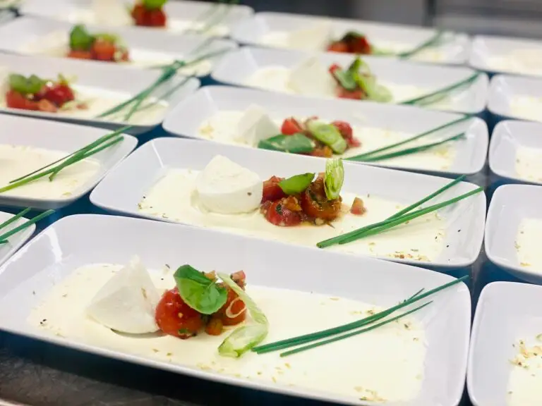 Reihe länglicher weisser Platten mit angerichtetem Zwischengang aus Mozzarella, Tomate und Kräutern