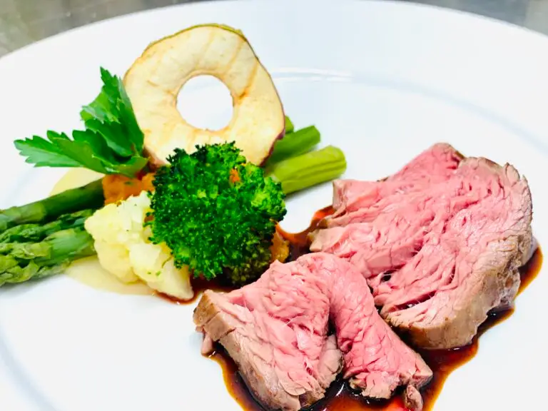 Teller mit rosa gebratenem Roastbeef an Jus, dazu grüner Spargel, Broccoli, Blumenkohl und eine gebratene Ananasscheibe