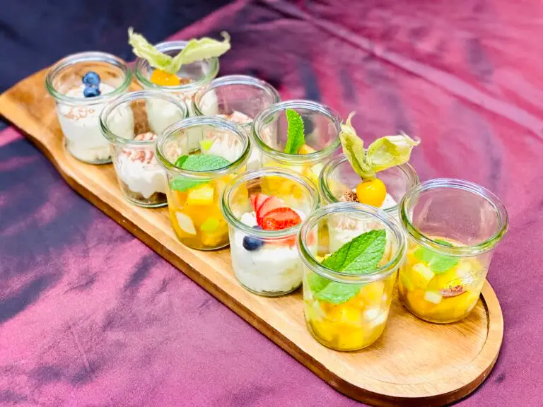 Neun Dessert-Gläschen mit Rahm, Mango, Beeren und Minze auf einem Holzbrett