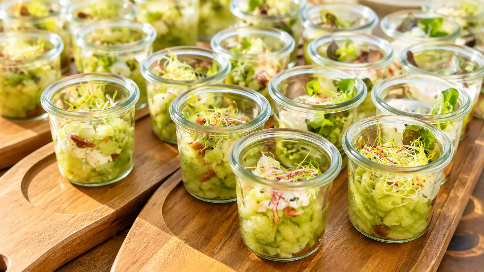 Holzbretter mit Gläschen voller Blattsalat, Gurken, Speck und Sprossen