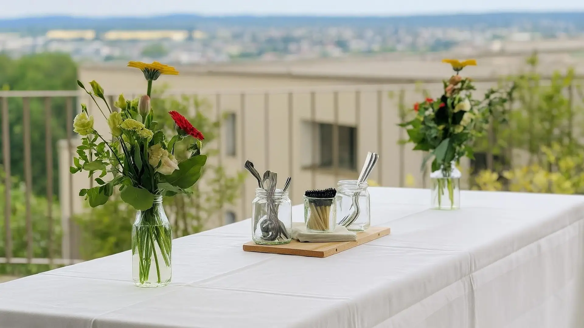 Weiss gedeckter Tisch mit zwei Blumenvasen und Knabbereien auf einer Terrasse mit weitem Blick über die Landschaft