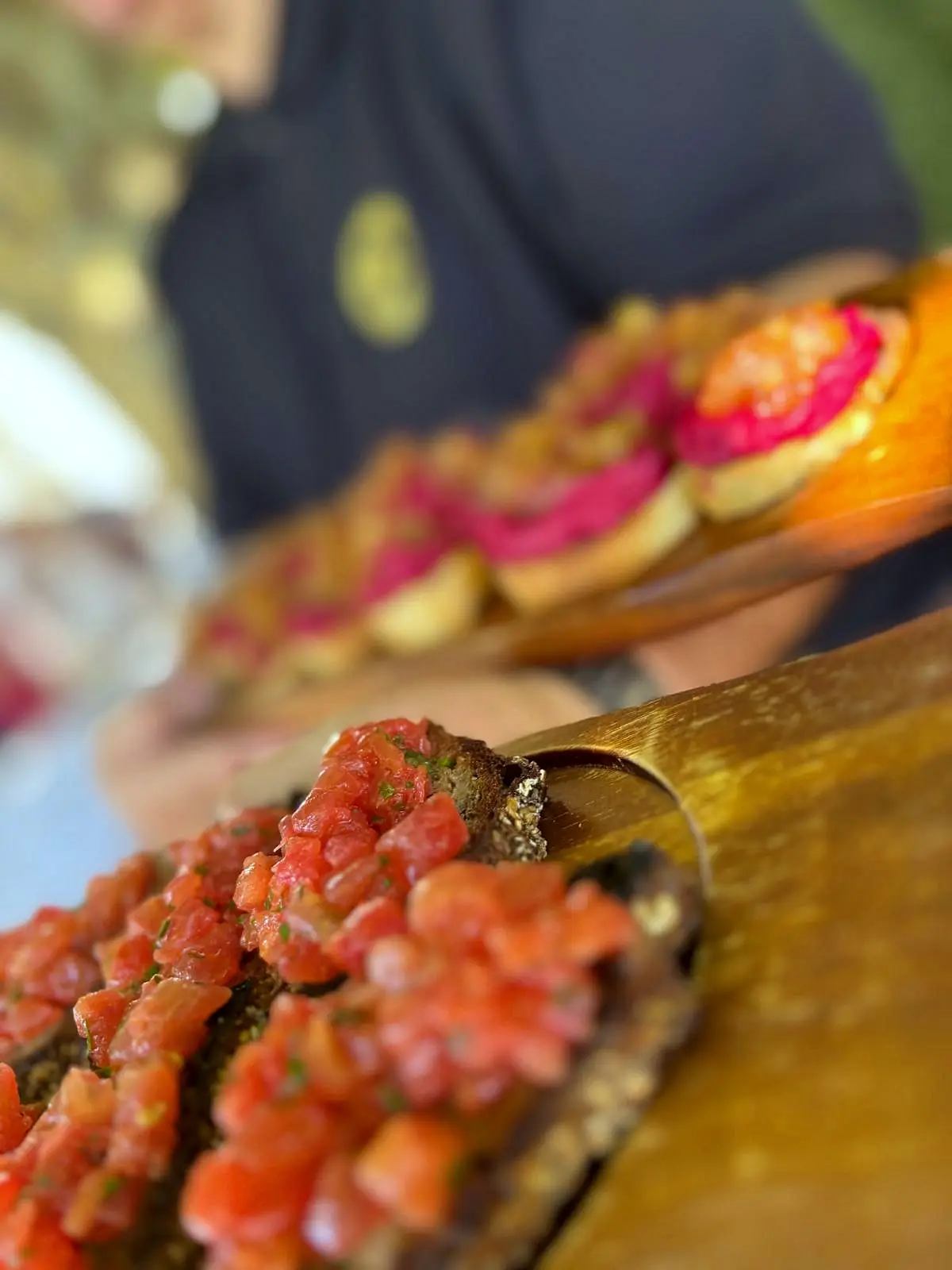 Nahaufnahme eines Servierbretts mit Crostini, belegt mit Tomatensalsa und Kräutern, gehalten von einer Servicekraft
