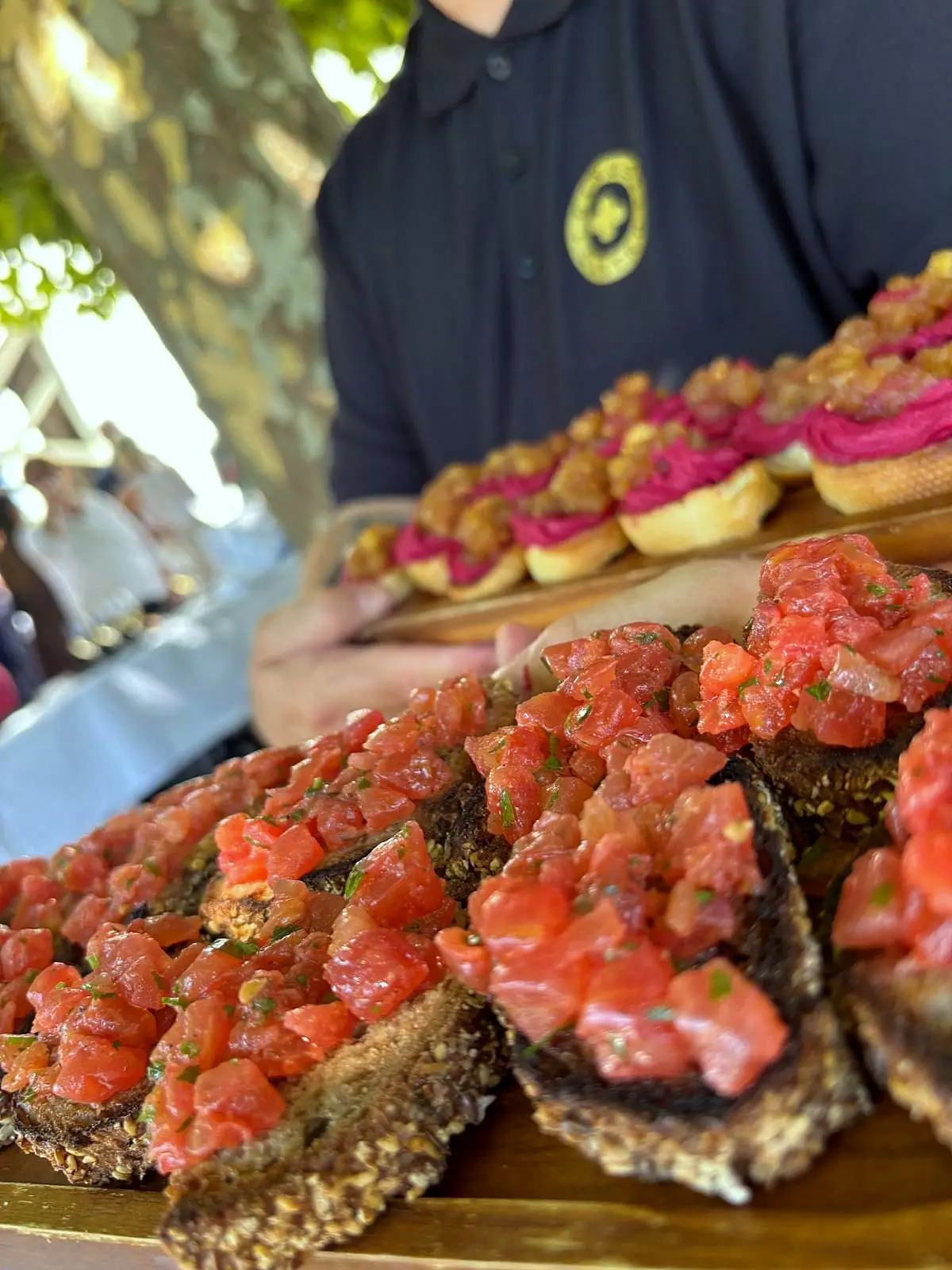 Mitarbeiter im dunklen Polo hält ein Holzbrett mit Crostini, belegt mit Tomatensalsa und Tatar
