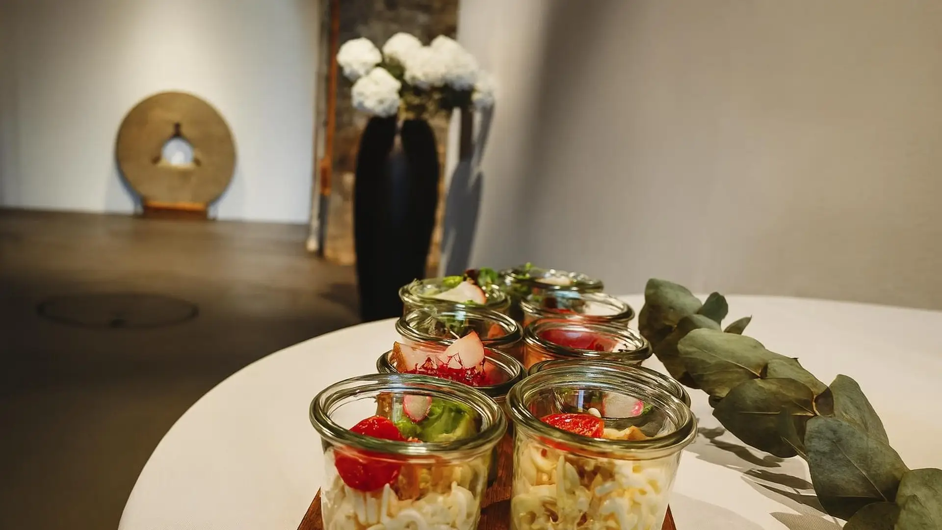 Runder weisser Tisch mit Gläschen voller Salat, Tatar und Erdbeeren, dazwischen Eukalyptuszweige als Deko