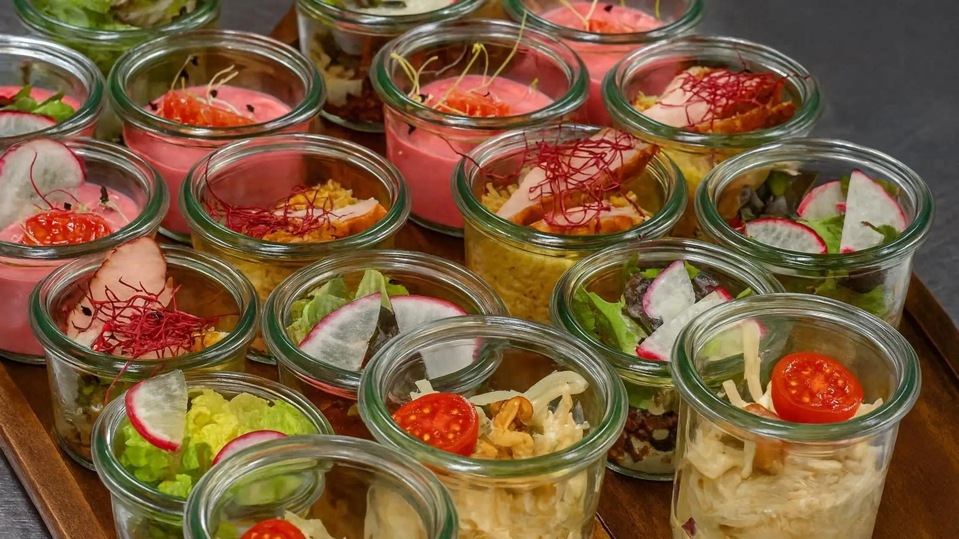 Dicht gestellte Gläschen mit Blattsalat, rosa Creme, Radieschenscheiben, Cherrytomaten und Chips