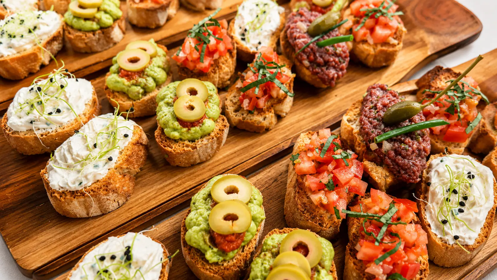Holzbretter mit belegten Crostini: Frischkäse mit Kresse, Avocadocreme mit Olive und Tomatensalsa mit Kräutern