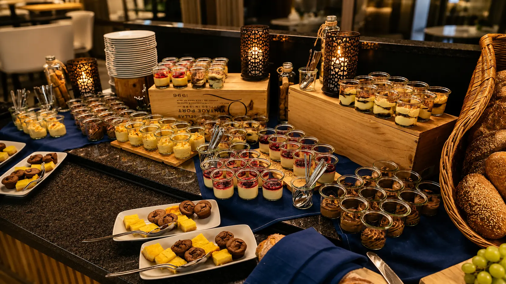 Dunkle Theke mit Dessert-Buffet: Gläschen mit Cremes und Beeren, kleine Törtchen, Brot, Trauben und Windlichter