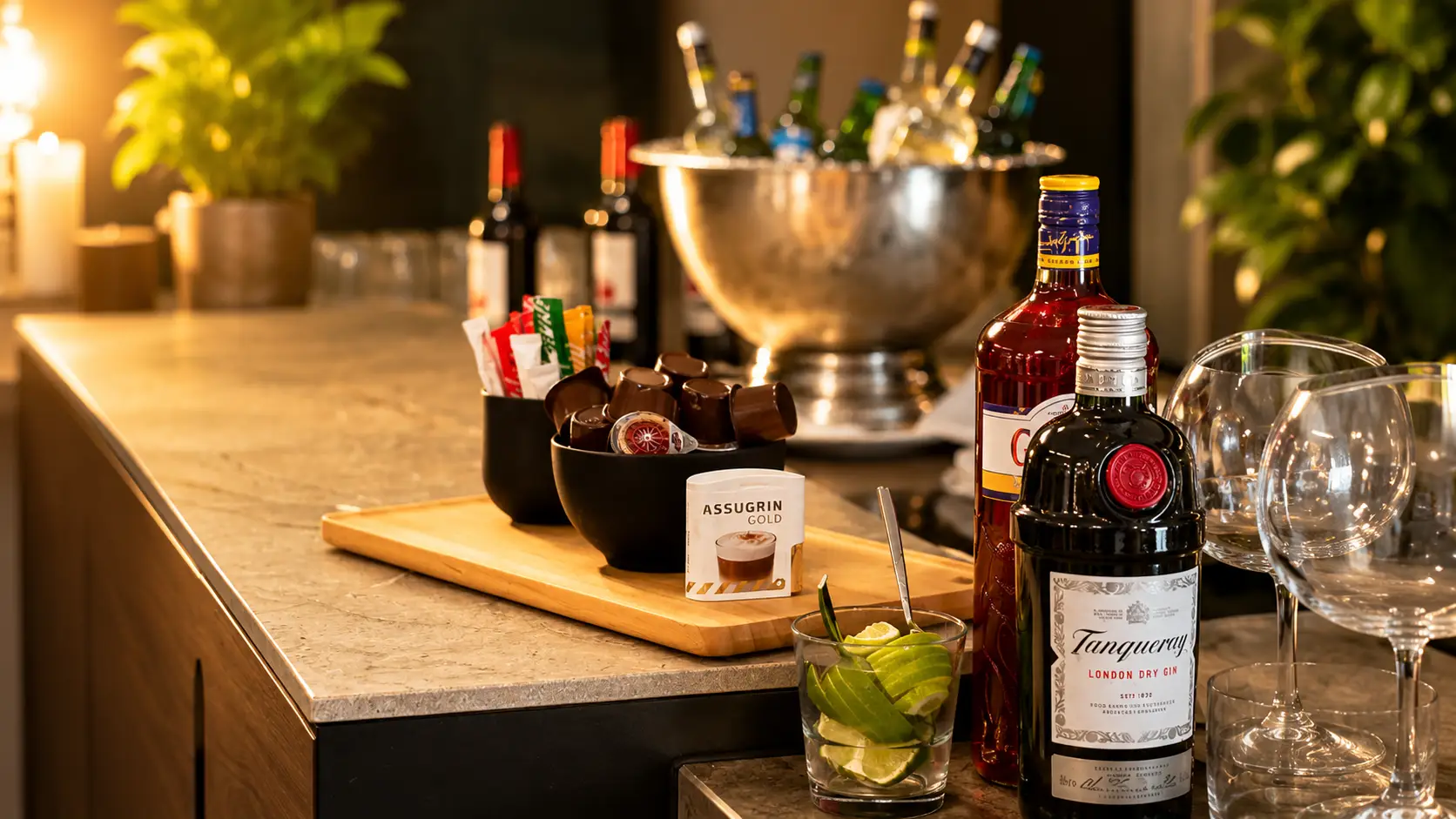 Aufgebaute Bar mit Spirituosen- und Weinflaschen, silbernem Sektkübel, Weingläsern, Oliven im Schälchen und Limettenscheiben