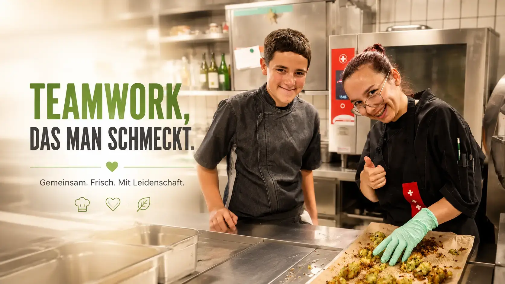Zwei Lernende in schwarzer Kochjacke an der Chromstahlanrichte mit einem Blech goldbrauner Gemüsetaler